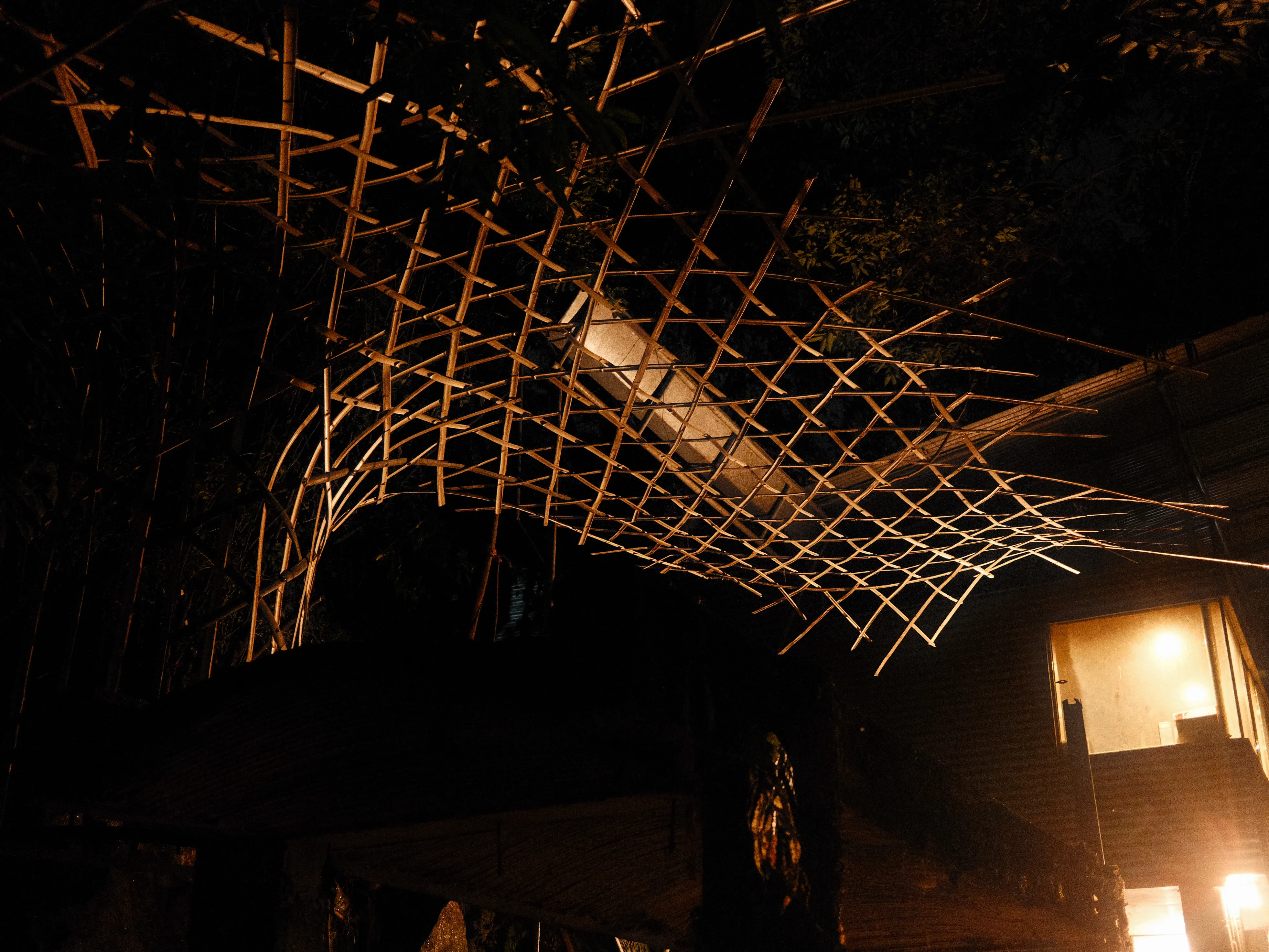 The completed bamboo pavilion illuminated at night by light from the studio
